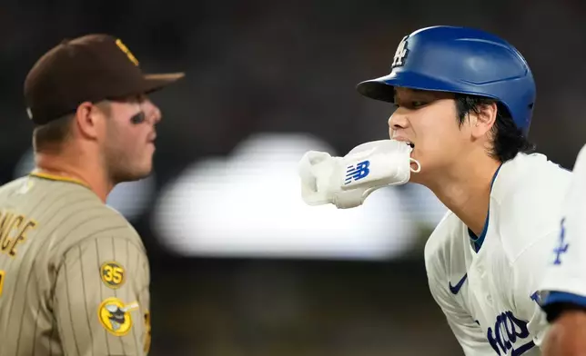 Los Angeles Dodgers' Shohei Ohtani, right, holds his batting guard in his teeth after hitting a single as he waits for a batboy to take it while San Diego Padres first baseman Ty France stands by during the first inning of a baseball game Wednesday, Sept. 23, 2026, in Los Angeles. (AP Photo/Mark J. Terrill)