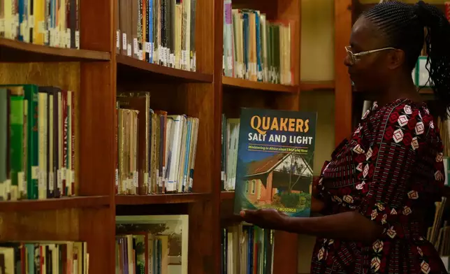 Linet Mmbone, an assistant librarian at the Friends Theological College holding out a book from the shelf, in Kaimosi, Kenya, Saturday, Sept. 19, 2026. (AP Photo/Jackson Njehia)