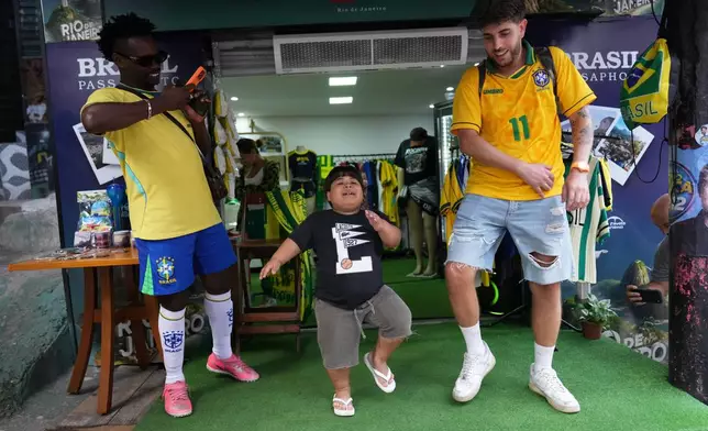 Influencer Narutinho, center, dances with Spain's tourist Ricard Sastre, right, at the Rocinha favela in Rio de Janeiro, on Sept. 2, 2026. (AP Photo/Silvia Izquierdo)