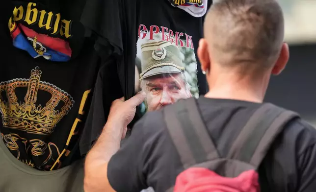 A buyer checks a T-shirt with a picture of former Bosnian Serb wartime general Ratko Mladic displayed on Belgrade's main pedestrian street, Serbia, Friday, Sept. 4, 2026. (AP Photo/Darko Vojinovic)