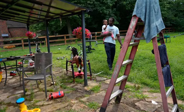 Khalidou Sy, a Mauritanian immigrant, carries his young daughter in the backyard of the family's home in Lockland, Ohio, Friday, July 31, 2026. (AP Photo/Carolyn Kaster)