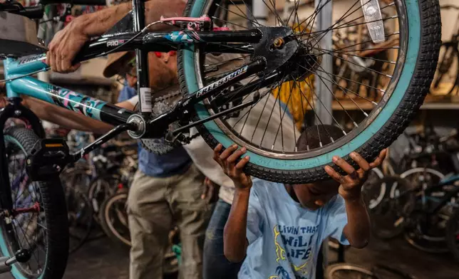 Vincent Wilson, left, who takes in donated, broken bikes and offers them up in the community to anyone who helps fix them up, repairs a bike with the help a seven-year-old boy at Bikes and Stuff in Lockland, Ohio, Friday, July 10, 2026. (AP Photo/Carolyn Kaster)