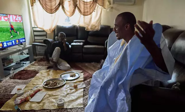 Samba Diallo, right, wears his daraa, a traditional robe worn in his homeland, Mauritania, after eating a communal meal of lamb and bread on the floor of his apartment with his roommate, Alassane Sow, in Lockland, Ohio, Friday, July 17, 2026. Diallo is part of an unprecedented migration surge, and an Associated Press analysis of exclusive data shows they turned some of the unlikeliest of places, like Lockland, into new American melting pots. (AP Photo/Carolyn Kaster)