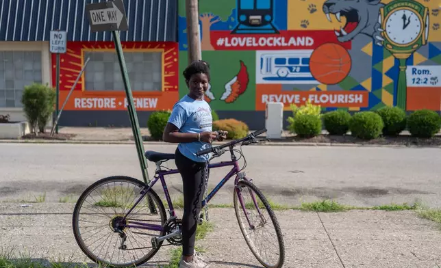 Halimata Ndiaye pauses on the new purple bike she just received from Bikes and Stuff in Lockland, Ohio, Friday, July 10, 2026. The shop offers free bikes to anyone willing to help refurbish one and has become the center of life for the West African community here. (AP Photo/Carolyn Kaster)