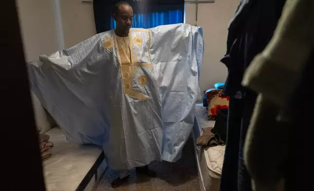 Samba Diallo displays his daraa, a loose-fitting traditional robe worn by men in Mauritania, as he stands in the bedroom of his shared apartment in Lockland, Ohio, Friday, July 17, 2026. Diallo, like many Mauritanians, spent weeks making his way through a half-dozen countries on buses, on foot, through the jungle and across rivers, until he finally walked across the U.S. southern border and asked for asylum. (AP Photo/Carolyn Kaster)