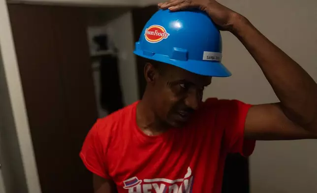 Samba Diallo, a Mauritanian immigrant, tries on a work safety helmet in a bedroom of his shared apartment in Lockland, Ohio, Friday, July 17, 2026. Diallo, like many from Mauritania, had fled a country where he was persecuted for opposing the country’s repressive government. (AP Photo/Carolyn Kaster)