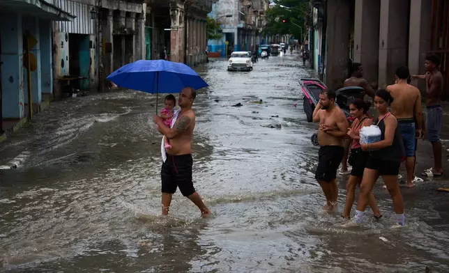 People wade through a flooded street as a man protects a girl from the rain with an umbrella in Havana, Wednesday, Sept. 23, 2026. (AP Photo/Ramon Espinosa)