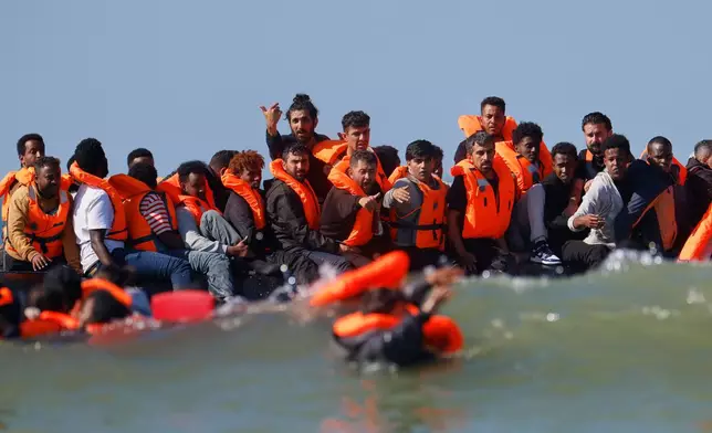 A group of migrants on a boat wave to others still in the water as they try to cross the channel from France to Britain on a dinghy boat, in Hardelot, northern France, Wednesday, Sept. 23, 2026. (AP Photo/Jean-Francois Badias)