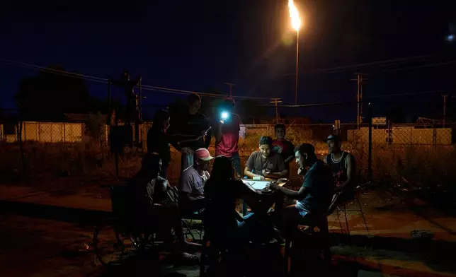 People play dominoes under the light of a cell phone flashlight, near a gas flare during a power outage in Cabimas, Venezuela, Monday, Aug. 31, 2026. (AP Photo/Ariana Cubillos)