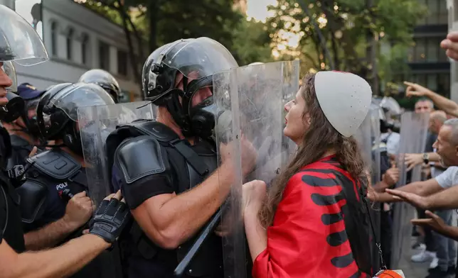 A woman draped in an Albanian flag clashes with police officers during ongoing demonstrations against plans for a luxury resort in a protected coastal area linked to Jared Kushner, U.S. President Donald Trump's son-in-law, in Tirana, Albania, Tuesday, Sept. 8, 2026. (AP Photo/Hameraldi Agolli)