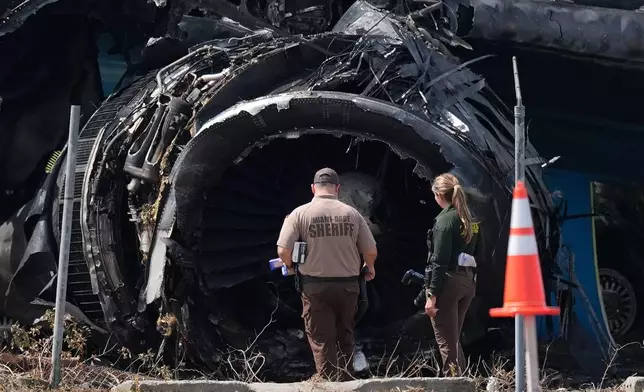 Law enforcement officers walk in front of a destroyed engine as they inspect an Amazon cargo plane two days after it overshot a runway at Miami International Airport, Tuesday, Sept. 8, 2026, in Miami. (AP Photo/Rebecca Blackwell)