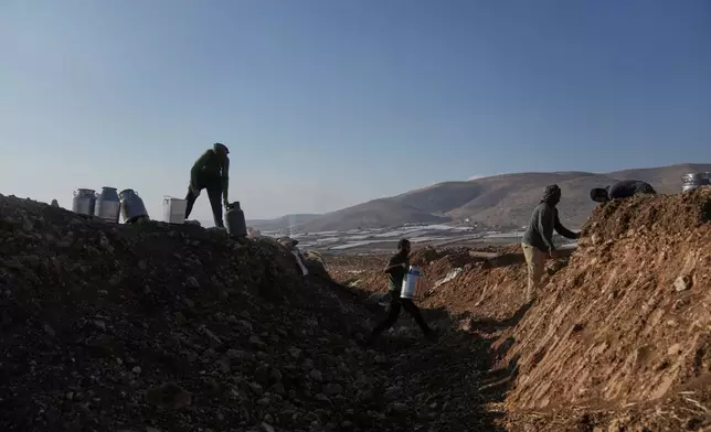Palestinian farmers carry containers of milk from their livestock across a trench dug by the Israeli army in a road leading to the West Bank hamlet of Khirbet Ras al-Ahmar, southeast of Tubas, on their way to sell it Saturday, Sept. 19, 2026. (AP Photo/Majdi Mohammed)