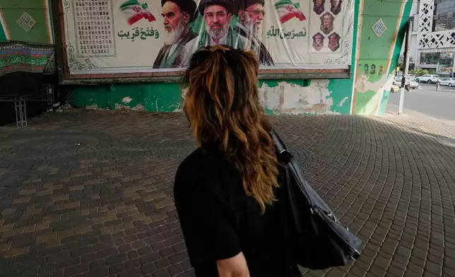 A woman walks past a banner showing portraits of the late Iranian revolutionary founder Ayatollah Khomeini, left, Supreme Leader Ayatollah Mojtaba Khamenei, center, and the late Supreme Leader Ayatollah Ali Khamenei in northern Tehran, Iran, Saturday, Sept. 12, 2026. (AP Photo/Vahid Salemi)