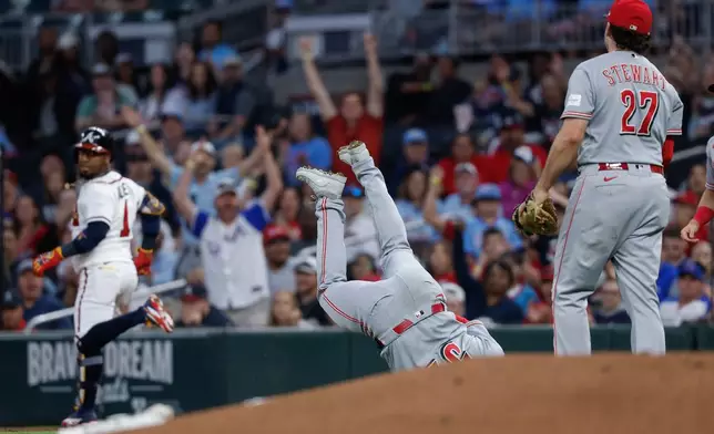 Cincinnati Reds pitcher Brady Singer, center, flips over first baseman Sal Stewart (27) while fielding a single hit by Atlanta Braves' Ozzie Albies (1) during the first inning of a baseball game, Thursday, Sept. 24, 2026, in Atlanta. (AP Photo/Erik S. Lesser)