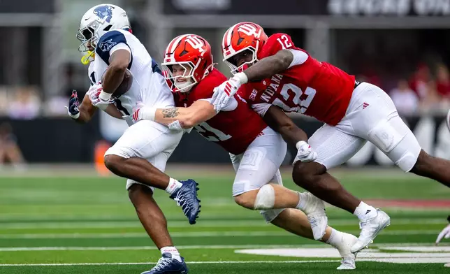 Howard running back John Washington IIl, left, is contacted by Indiana linebacker Jacob Savage, center, and defensive end Tobi Osunsanmi (12) during the second half an NCAA college football game, Saturday, Sept. 12, 2026, in Bloomington, Ind. (AP Photo/Doug McSchooler)