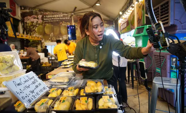 A worker livestreams while selling durians at a durian stall in Petaling Jaya, on the outskirts of Kuala Lumpur, Malaysia, Monday, June 22, 2026. (AP Photo/Vincent Thian)