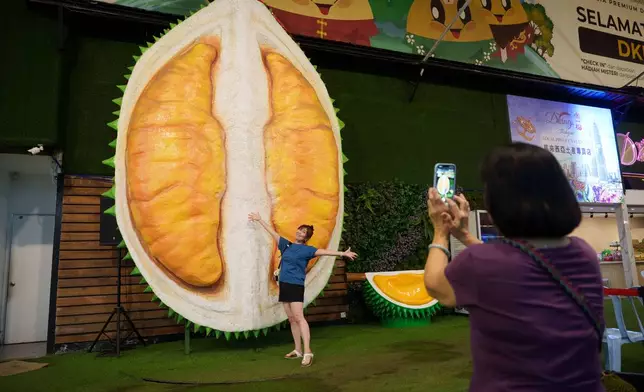 A customer poses beside a giant durian display at a durian stall in Petaling Jaya, on the outskirts of Kuala Lumpur, Malaysia, Monday, June 22, 2026. (AP Photo/Vincent Thian)