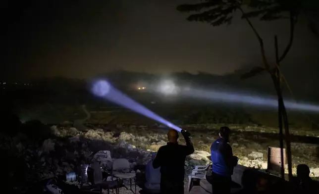 A Palestinian scans a valley with a flashlight as cars move on the top of a hill during a volunteer night watch to help prevent Israeli settler attacks in the West Bank town of Sinjil, Wednesday, Sept. 2, 2026. (AP Photo/Leo Correa)