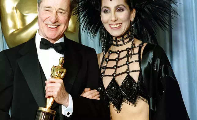 FILE - Actress-singer Cher wears a creation by designer Bob Mackie as she poses with actor Don Ameche after presenting him with the Oscar for best supporting actor at the Academy Awards in Los Angeles, on March 24, 1986. (AP Photo/Lennox McLendon, File)