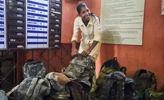 A student smiles after locating her bag from a pile extracted from the mud brought in by the recent flash floods, at the Shree Bagheswori Madhyamik School in Galchhi, Dhading district of Nepal Sunday, Aug. 30, 2026. (AP Photo/Niranjan Shrestha)