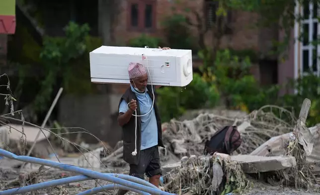 A resident carries an air cooler salvaged from his damaged house after flash flooding in the Devighat area of Nuwakot district, Nepal, Saturday, Aug. 29, 2026. (AP Photo/Rajesh Kumar Singh)
