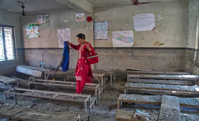 A parent searches for her child's belongings inside a flood-damaged classroom at the Shree Bagheswori Madhyamik School in Galchhi, Dhading district of Nepal Sunday, Aug. 30, 2026. (AP Photo/Niranjan Shrestha)