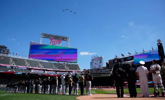 Fans and members of the military stand for the playing of the national anthem as planes perform a flyover prior to a baseball game between the Minnesota Twins and the Cleveland Guardians, Sunday, Sept. 13, 2026, in Minneapolis. (AP Photo/Joseph Scheller)