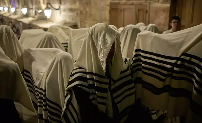 Covered in prayer shawls, Jewish men pray in front of the gate at Souq Al-Qattanin, or Cotton Merchants' Market, one of the entrances to the Al-Aqsa Mosque compound in the Old City of Jerusalem, Monday, Sept. 28, 2026, during morning prayers for the Jewish holiday of Sukkot. (AP Photo/Leo Correa)