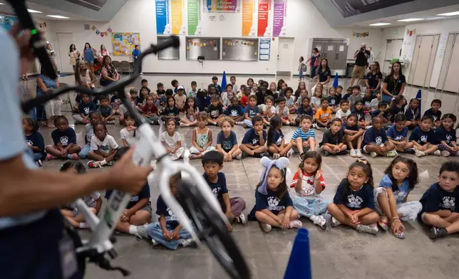 Physical education teacher Ray Herrera demonstrates how to ride a bike as students gather for a learn-to-ride program at Terra Vista Elementary School in Rancho Cucamonga, Calif., Wednesday, Sept. 2, 2026. (AP Photo/Jae C. Hong)