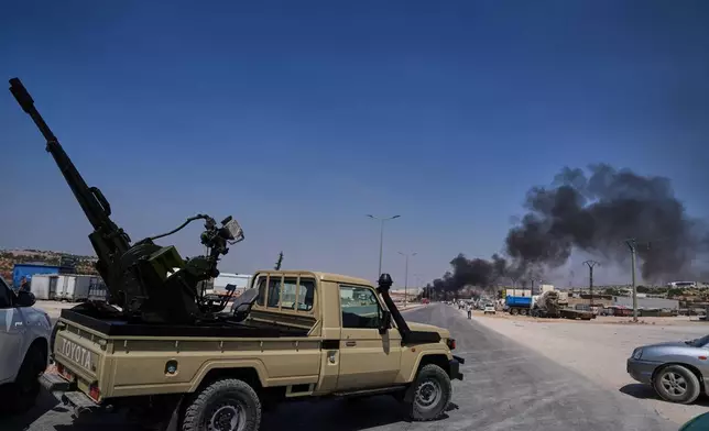 A pickup truck fitted with an anti-aircraft gun is parked across a road as smoke rises after an explosion at what state media said was a weapons depot in the Burj al-Nimra area near Sarmada, in Idlib province, Syria, Wednesday, Sept. 9, 2026.(AP Photo/Omar Albam)