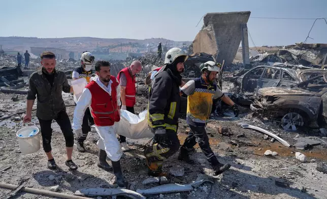 Civil defense workers and a firefighter remove a body from the site of an explosion at what Syria's Defense Ministry said was a warehouse used for the temporary storage of weapons near Sarmada, in Idlib province, Syria, Wednesday, Sept. 9, 2026. (AP Photo/Omar Albam)