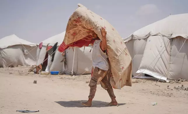 A displaced Yemeni carries a carpet at Al-Firdaws camp in Ras Imran, just outside Aden, Yemen, Monday, Sept. 14, 2026. (AP Photo/Abdulnasser Alseddik)
