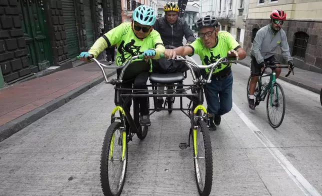 A volunteer with the "Ciegocleta" initiative, right, pushes a tandem bike for two visually impaired participants bicycle in Quito, Ecuador, Sunday, Aug. 30, 2026. (AP Photo/Dolores Ochoa)