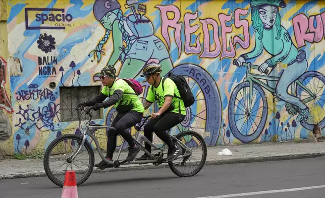 A volunteer with the "Ciegocleta" initiative, left, guides a visually impaired participant on a tandem bicycle in Quito, Ecuador, Sunday, Aug. 30, 2026. (AP Photo/Dolores Ochoa)