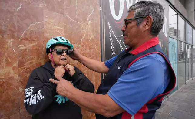 A volunteer helps a visually impaired participant put on a helmet before a bicycle ride with the "Ciegocleta" initiative in Quito, Ecuador, Sunday, Aug. 30, 2026. (AP Photo/Dolores Ochoa)