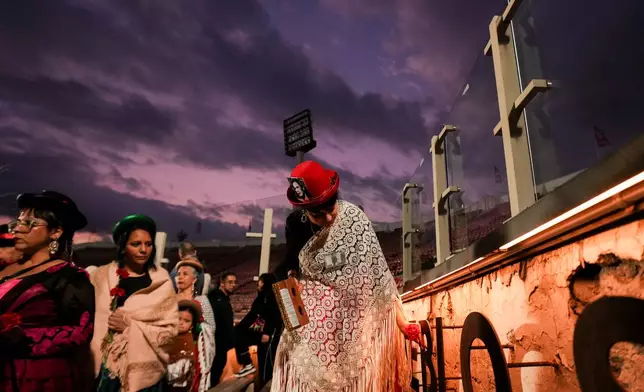 A dancer, wearing photos of detainees who disappeared during Chile's military dictatorship, places a flower at the National Stadium, which served as a detention and torture center in the early days of the regime, during an event marking the anniversary of the 1973 military coup that toppled the government of President Salvador Allende, in Santiago, Chile, Friday, Sept. 11, 2026. (AP Photo/Esteban Felix)