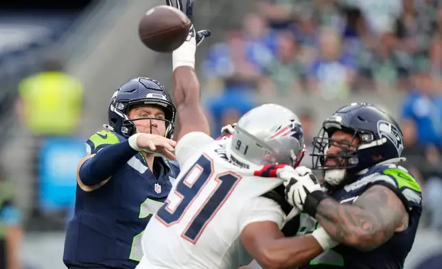 Seattle Seahawks quarterback Drew Lock, left, throws a pass under pressure as New England Patriots linebacker Elijah Ponder, center, reaches during the first half of an NFL football game, Wednesday, Sept. 9, 2026, in Seattle. (AP Photo/Stephen Brashear)