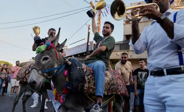 Kevin Nakhleh, 21, centre, rides his donkey, Al-Aawar, as he holds up a trophy after winning the traditional summer donkey race in Roum village, southern Lebanon, Sunday, Sept. 6, 2026. (AP Photo/Hussein Malla)