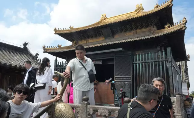 Visitors touch a crane statue near the Golden Hall in Wudang Mountains in central China's Hubei Province on Sept. 3, 2026. (AP Photo/Achmad Ibrahim)