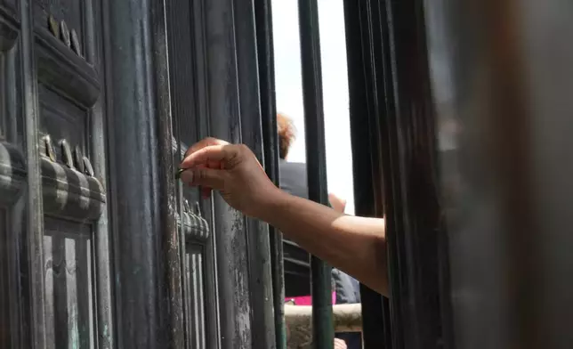 A visitor places a coin on the doors of the Golden Hall in Wudang Mountains in central China's Hubei Province on Sept. 3, 2026. (AP Photo/Achmad Ibrahim)