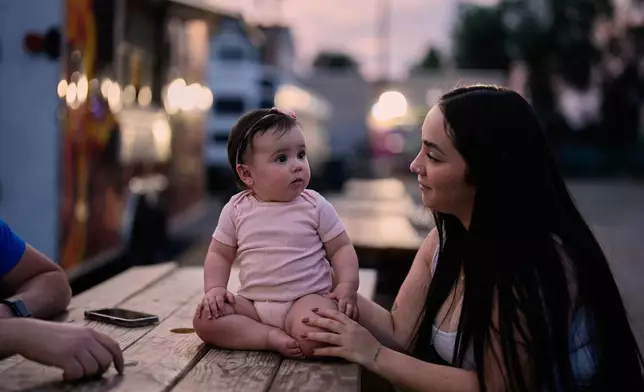 A Venezuelan mother sits with her daughter among food trucks Tuesday, July 14, 2026, in Midvale, Utah. (AP Photo/Gregory Bull)