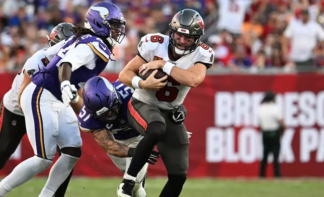 Tampa Bay Buccaneers quarterback Baker Mayfield (6) is tackled by Minnesota Vikings safety Joshua Metellus (44) and linebacker Blake Cashman (51) during the second half of an NFL football game in Tampa, Fla., Sunday, Sept. 27, 2026. (AP Photo/Jason Behnken)