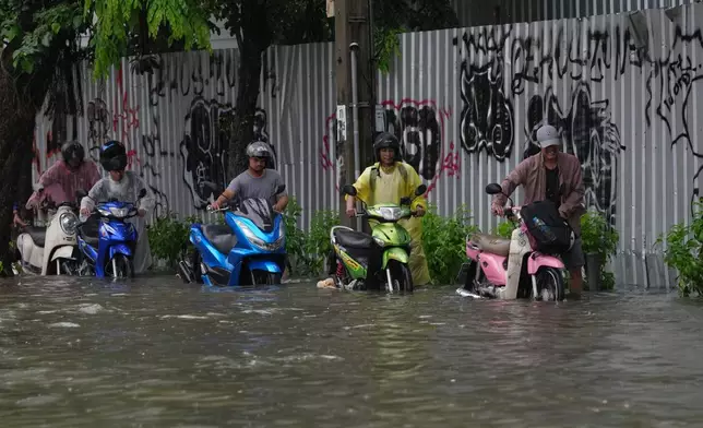 Men push motorcycles as they wade through floodwaters after heavy rain in Bangkok, Thailand Saturday, Sept. 26, 2026. (AP Photo/Sakchai Lalit)