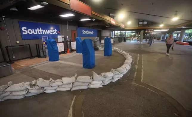 People walk past a closed ticket counter for Southwest Airlines lined with sandbags at Hilo International Airport as Hurricane Nolo sits nearby Friday, Sept. 25, 2026, in Hilo, Hawaii. (AP Photo/Gregory Bull)