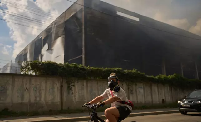 A local resident wears a gas mask as he rides a bicycle past a partially destroyed warehouse after a Russian drone attack in Brovary on the outskirts of Kyiv, Ukraine, Friday, Sept. 4, 2026. (AP Photo/Francisco Seco)