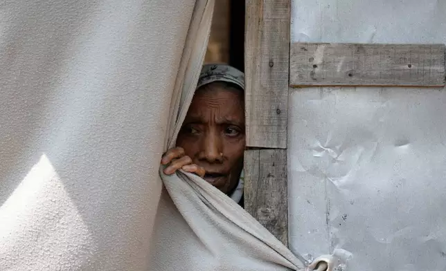 A Rohingya woman looks out from a blanket used as a wall at a temporary shelter where refugees live following government notices ordering the removal of unauthorized structures in Jammu, India, Wednesday, Sept. 16, 2026.(AP Photo/Channi Anand)