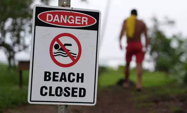 A lifeguard walks back to his tower after adjusting a beach closure sign as Hurricane Nolo sits nearby Saturday, Sept. 26, 2026, in Hilo, Hawaii. (AP Photo/Gregory Bull)