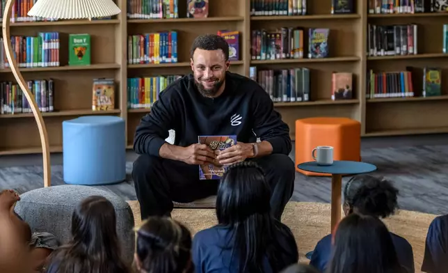 Warriors star Stephen Curry reads from the book, "Eye on the Ball" with students in the library during an event for his Eat.Learn.Play. Foundation at Madison Park Academy Primary in Oakland, Calif., on Wednesday, Sept. 23, 2026. (Carlos Avila Gonzalez/San Francisco Chronicle via AP)