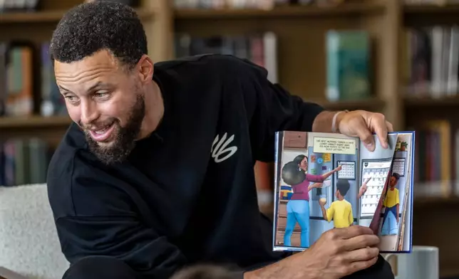 Warriors star Stephen Curry reads from the book, "Eye on the Ball" with students in the library during an event for his Eat.Learn.Play. Foundation at Madison Park Academy Primary in Oakland, Calif., on Wednesday, Sept. 23, 2026. (Carlos Avila Gonzalez/San Francisco Chronicle via AP)