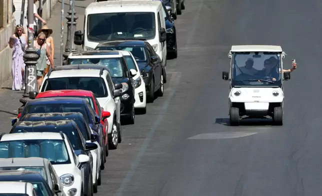A golf cart carrying tourists travels past parked cars in Rome, Tuesday, Aug. 18, 2026, as city officials move to regulate the rapidly growing industry amid complaints about congestion, illegal parking, and overtourism. (AP Photo/Gregorio Borgia)